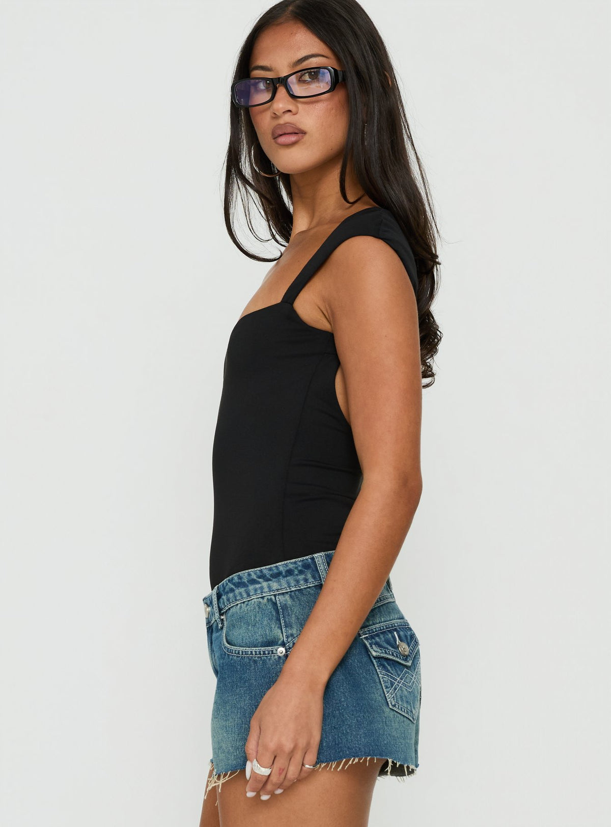 Featuring the Fabienna Scoop Neck Cap Sleeve Bodysuit in black with short sleeves side view of model wearing Princess Polly